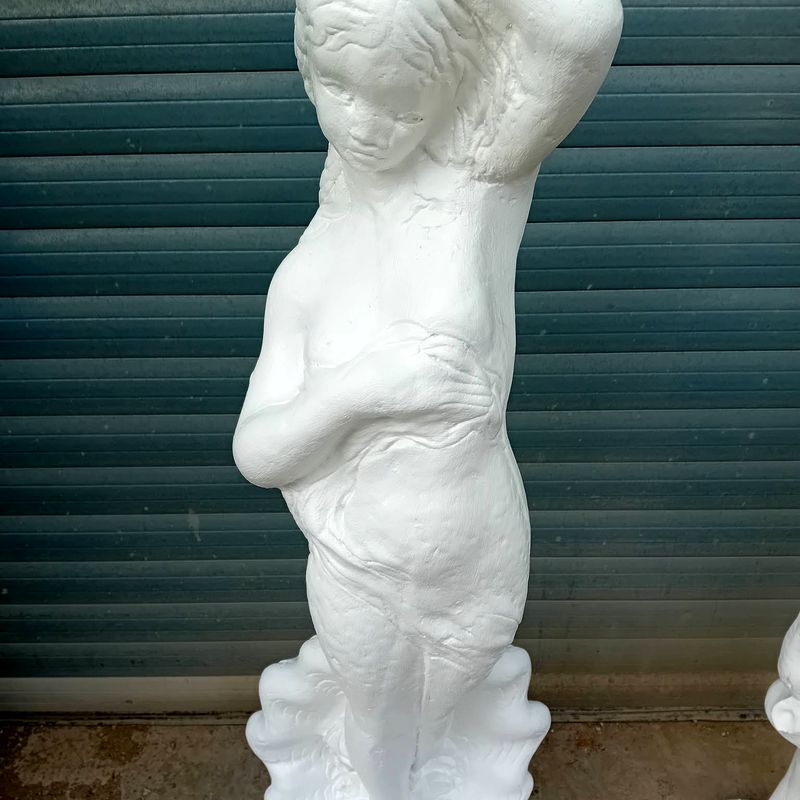 Tall classical statue of a woman in pale white concrete