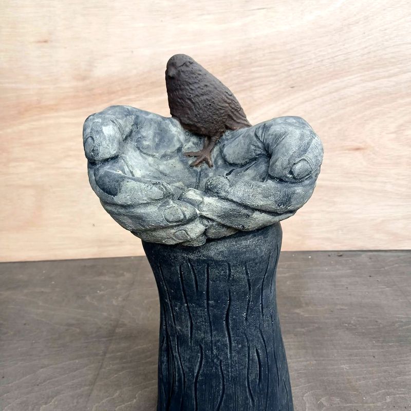 Pair of cupped stone hands holding a small bird, on a bark-textured column