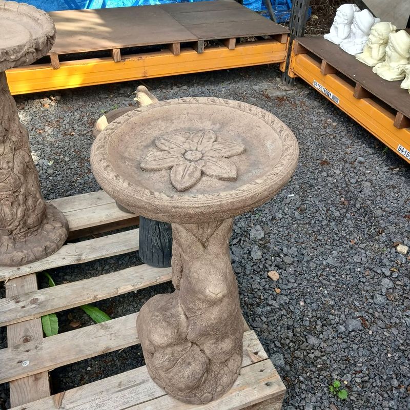 Bird bath with a flower motif in the bowl, on a tree-trunk base with a hare climbing it