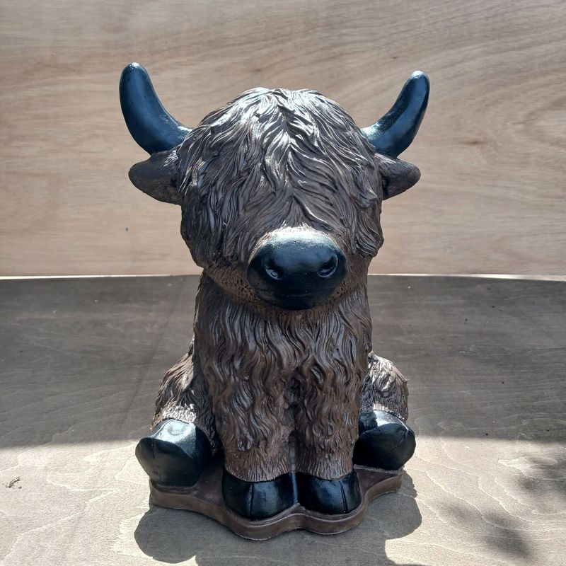 Seated Highland cow with shaggy brown coat and black horns and hooves, hand-painted concrete