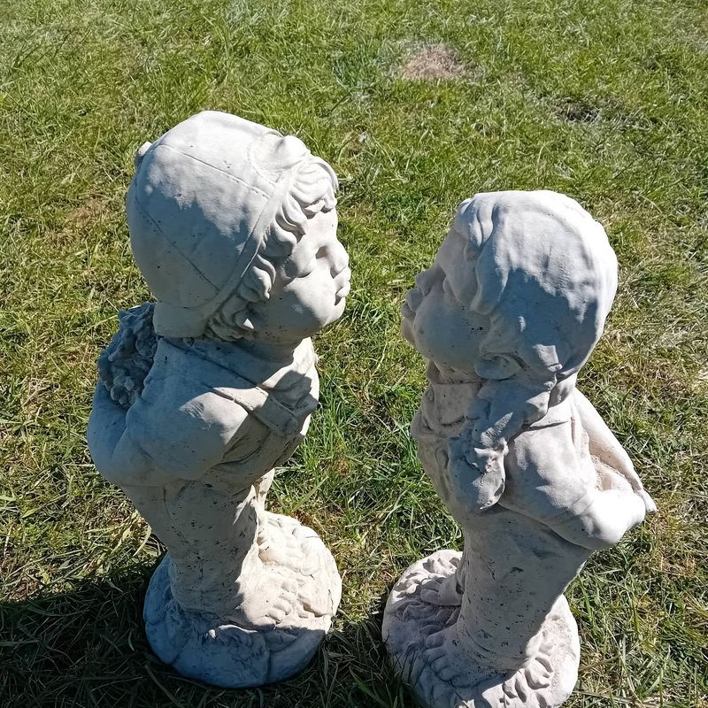 Pair of standing statues of a boy and girl leaning in for a kiss, on a lawn