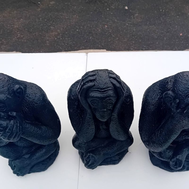 Black monkey statue covering its ears, with two matching monkeys partly in frame